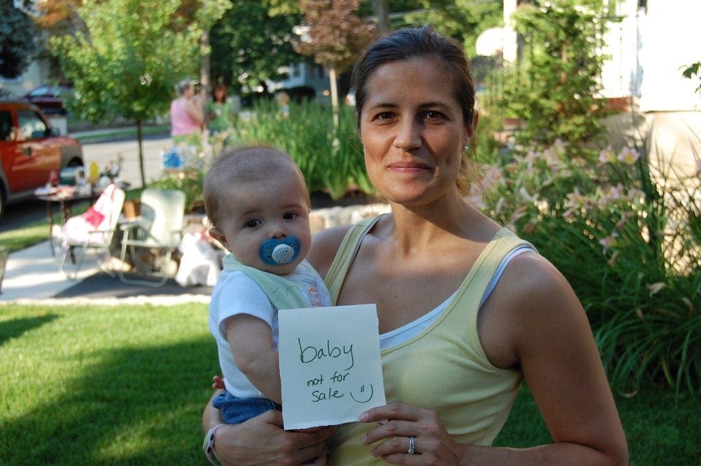 mother holding baby with sign saying baby not for sale
