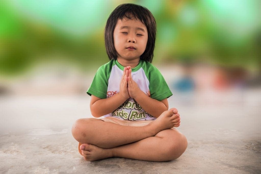 little girl sitting cross-legged saying a prayer