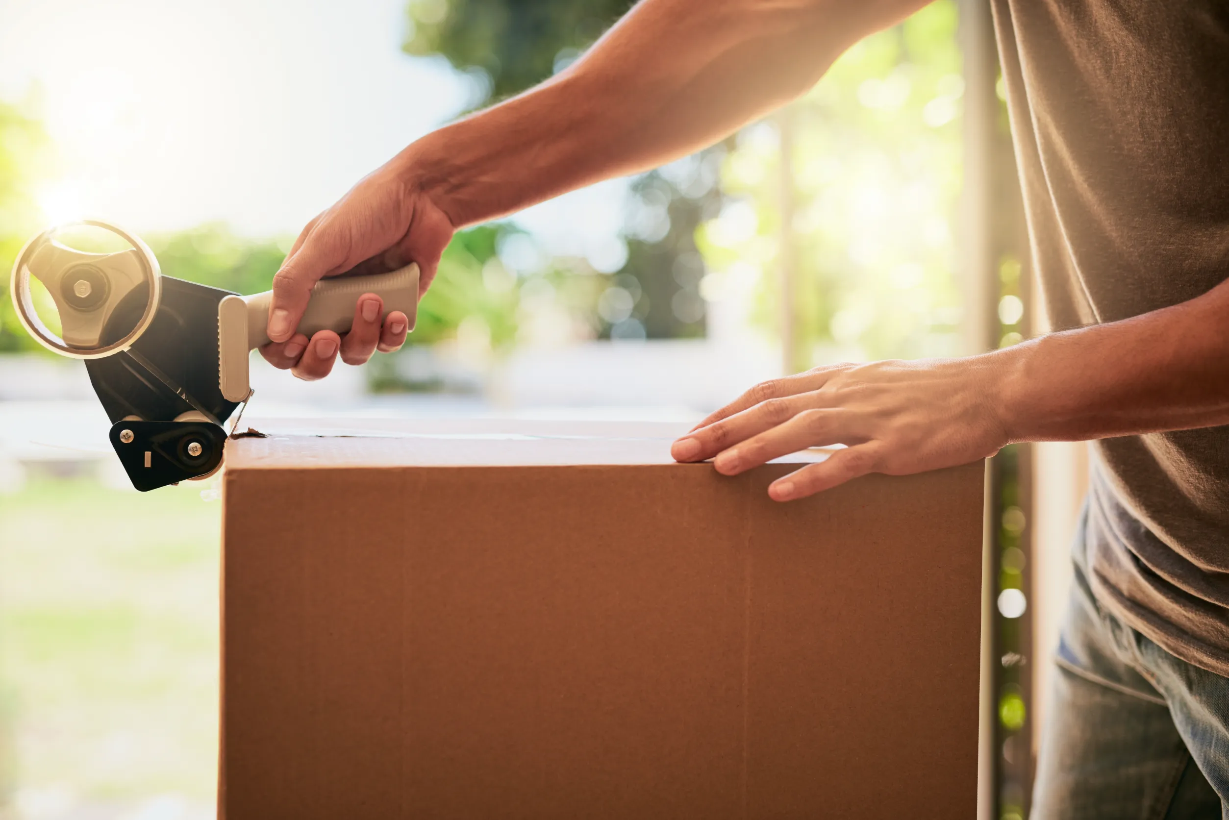 Closeup shot of an unrecognizable man closing a cardboard box with tape.