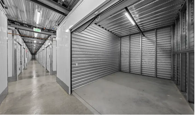 Empty Storage unit Long hallway of metal storage units in a self-storage facility, with an open unit on the right and bright overhead lighting.